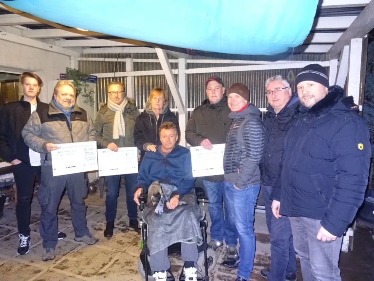 Gruppe von neun Personen, inkl. Mann im Rollstuhl, mit Spendenschecks, zeigt Solidarität und Gemeinschaft.